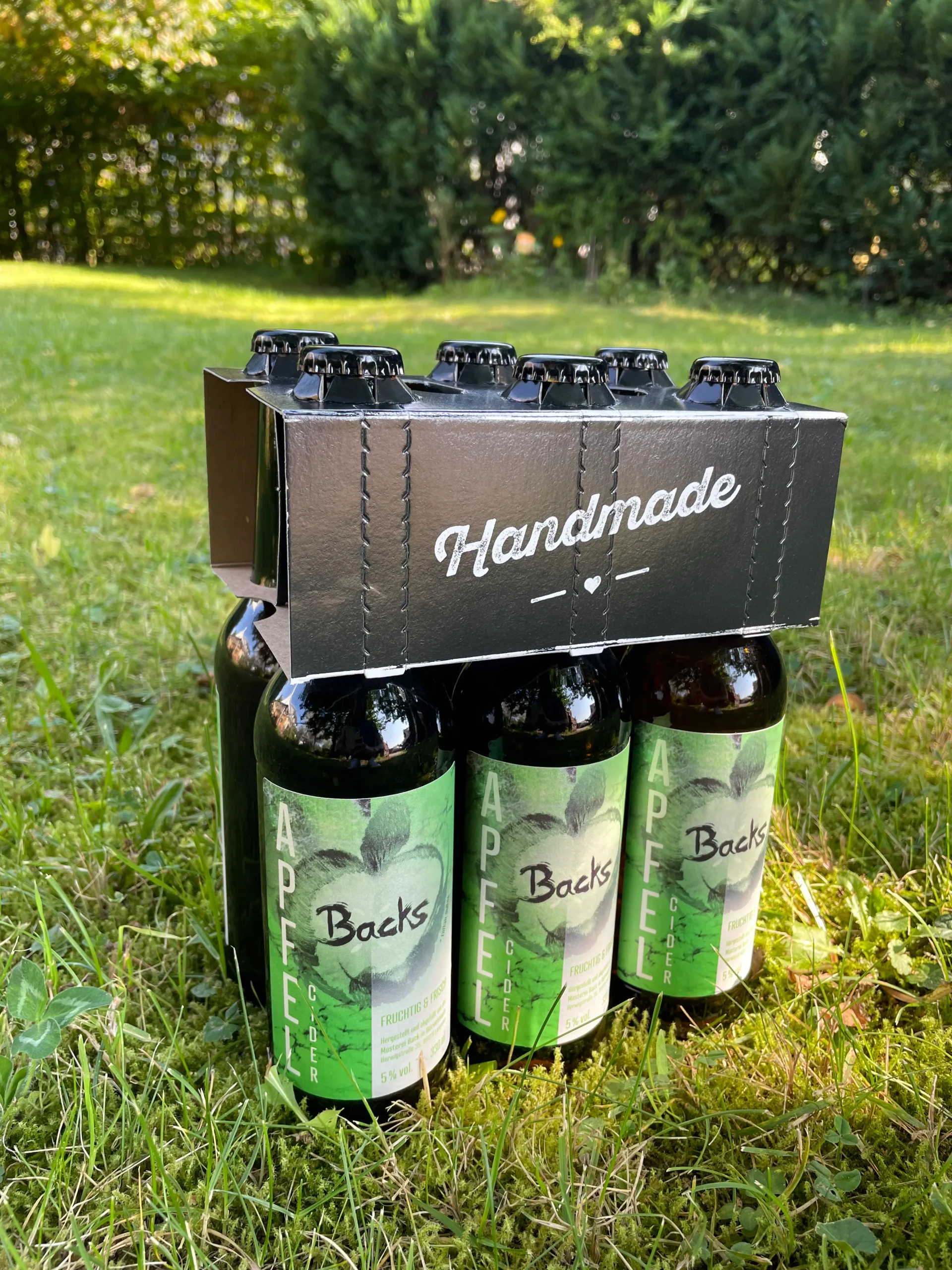 Sechs Flaschen Backs Apfel-Cider verpackt auf einer Wiese